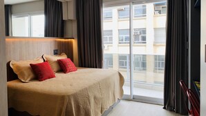 Una habitación de hotel moderna con una cama grande, un cabecero con iluminación ambiental, una puerta corredera de cristal a un balcón y vistas a la ciudad.