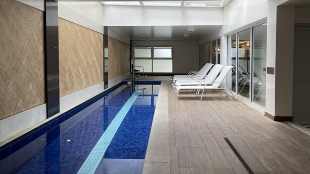 A modern indoor swimming pool with clear blue tiles, a wooden floor, and white sun loungers along the wall. - Hype055 in S o Paulo (São Paulo)