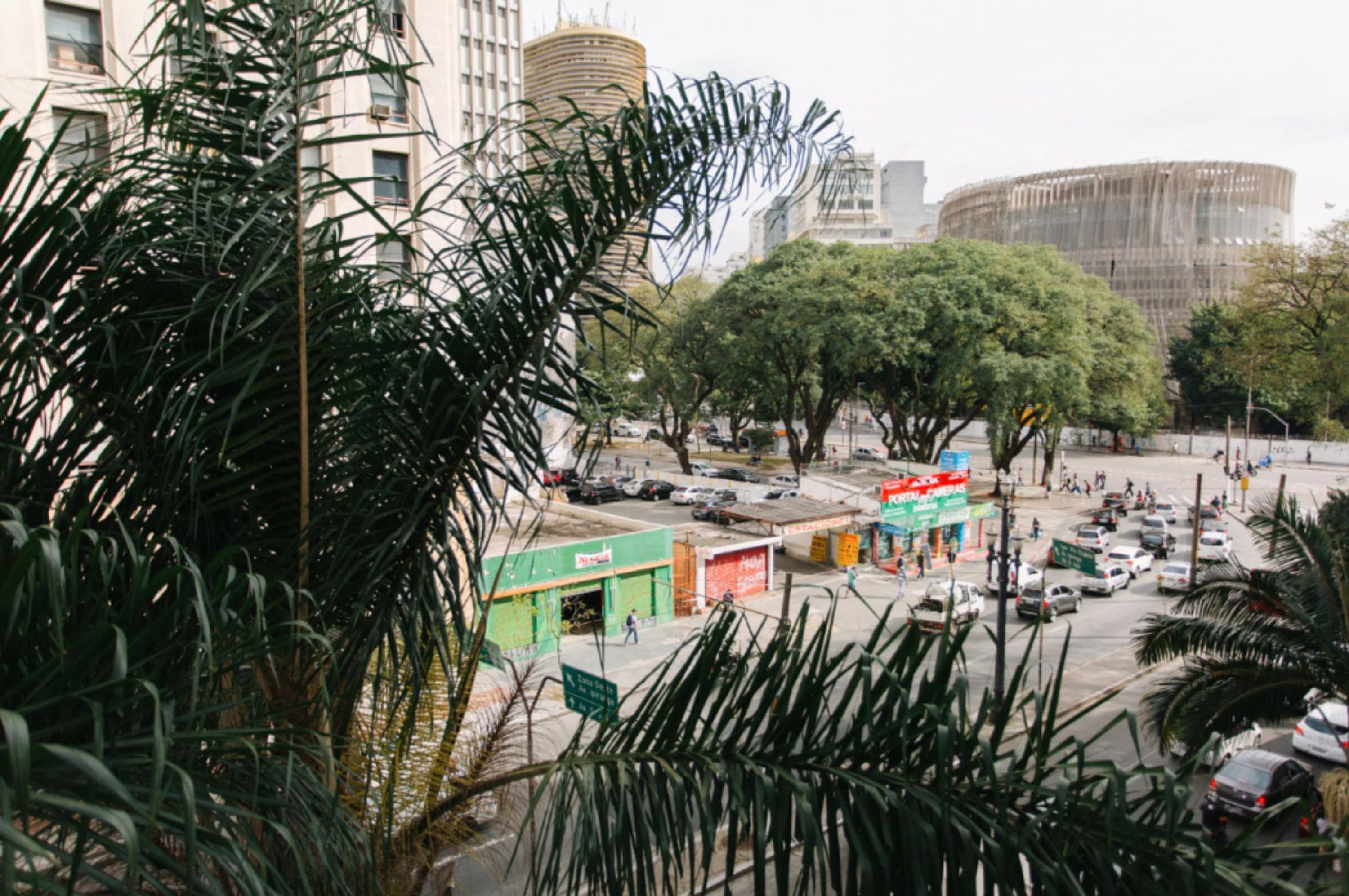 A busy urban street with palm trees, a round building, and various shops.
