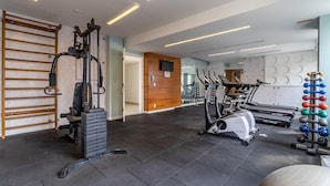 Un gimnasio con equipamiento de ejercicio, incluyendo una jaula para sentadillas, cintas de correr y una estación de levantamiento de pesas.