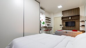 Una habitación de hotel moderna con una cama, un televisor montado en la pared, un pequeño rincón de estar con una mesa y un armario.