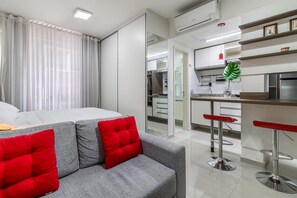 A modern hotel room with a grey sofa, red cushions, a small kitchen area, and a dining bar with red stools. - Av0108 in S o Paulo (São Paulo)
