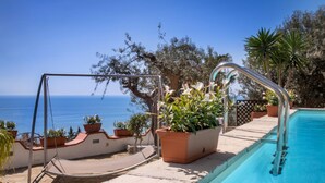 Ein Poolbereich mit Schaukelstuhl, Topfpflanzen und Blick aufs Meer.
