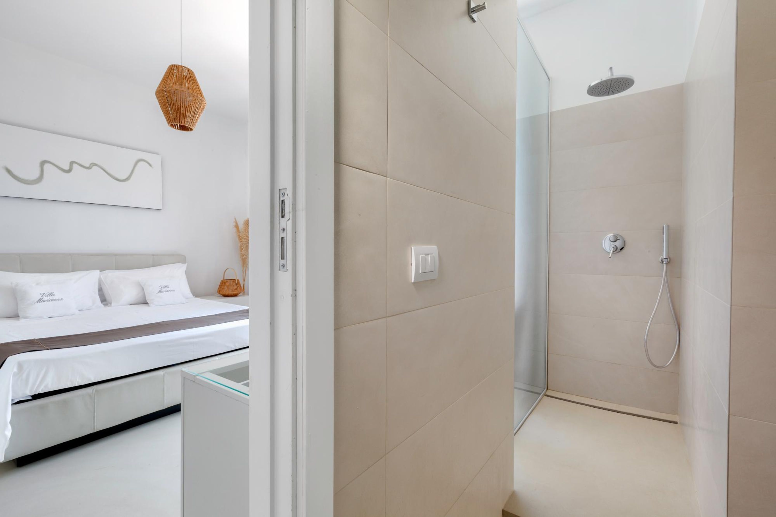 A modern bathroom with a glass shower enclosure, a bed with white linens, and a wall-mounted artwork.