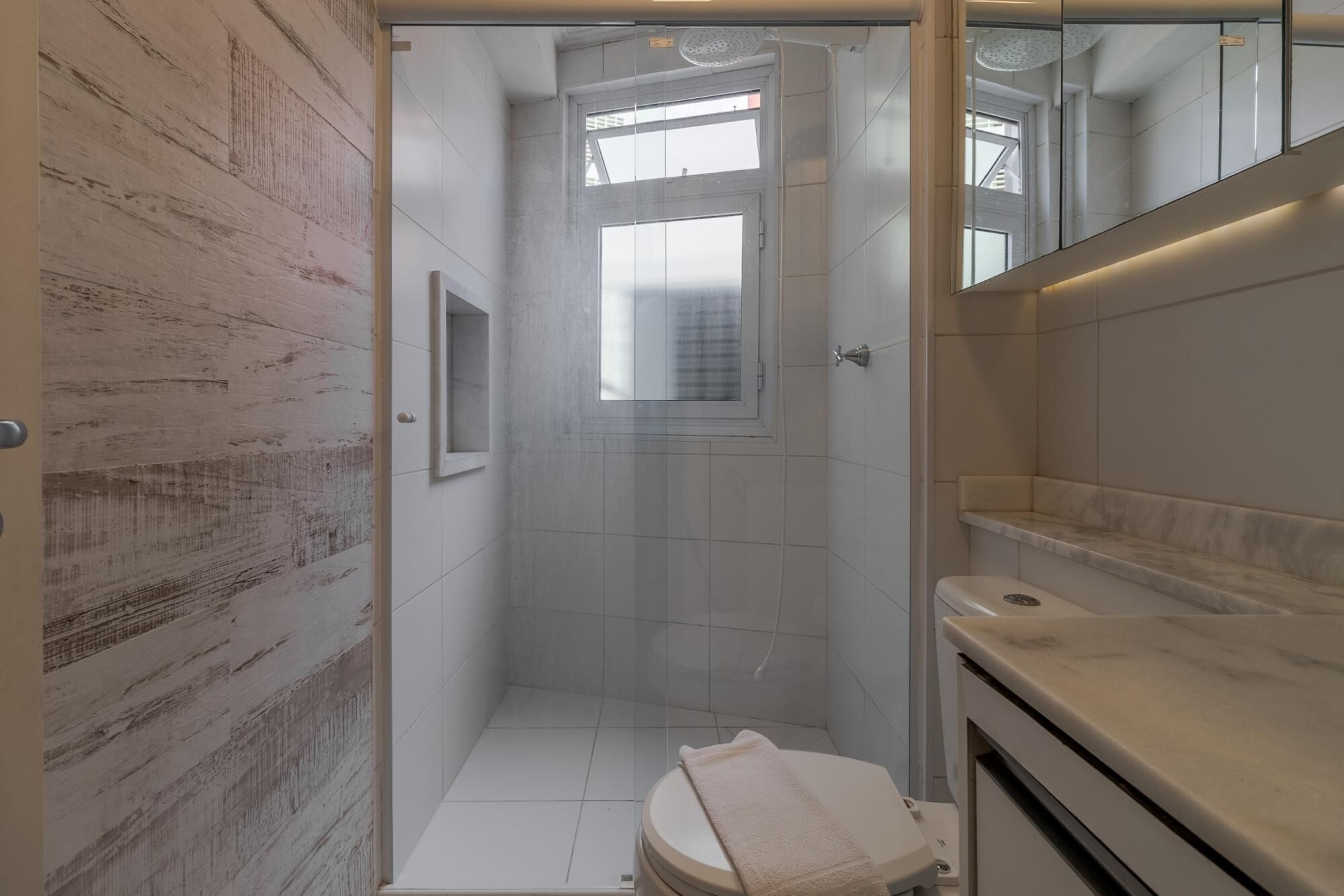 A bathroom with a shower, toilet, and a small window.