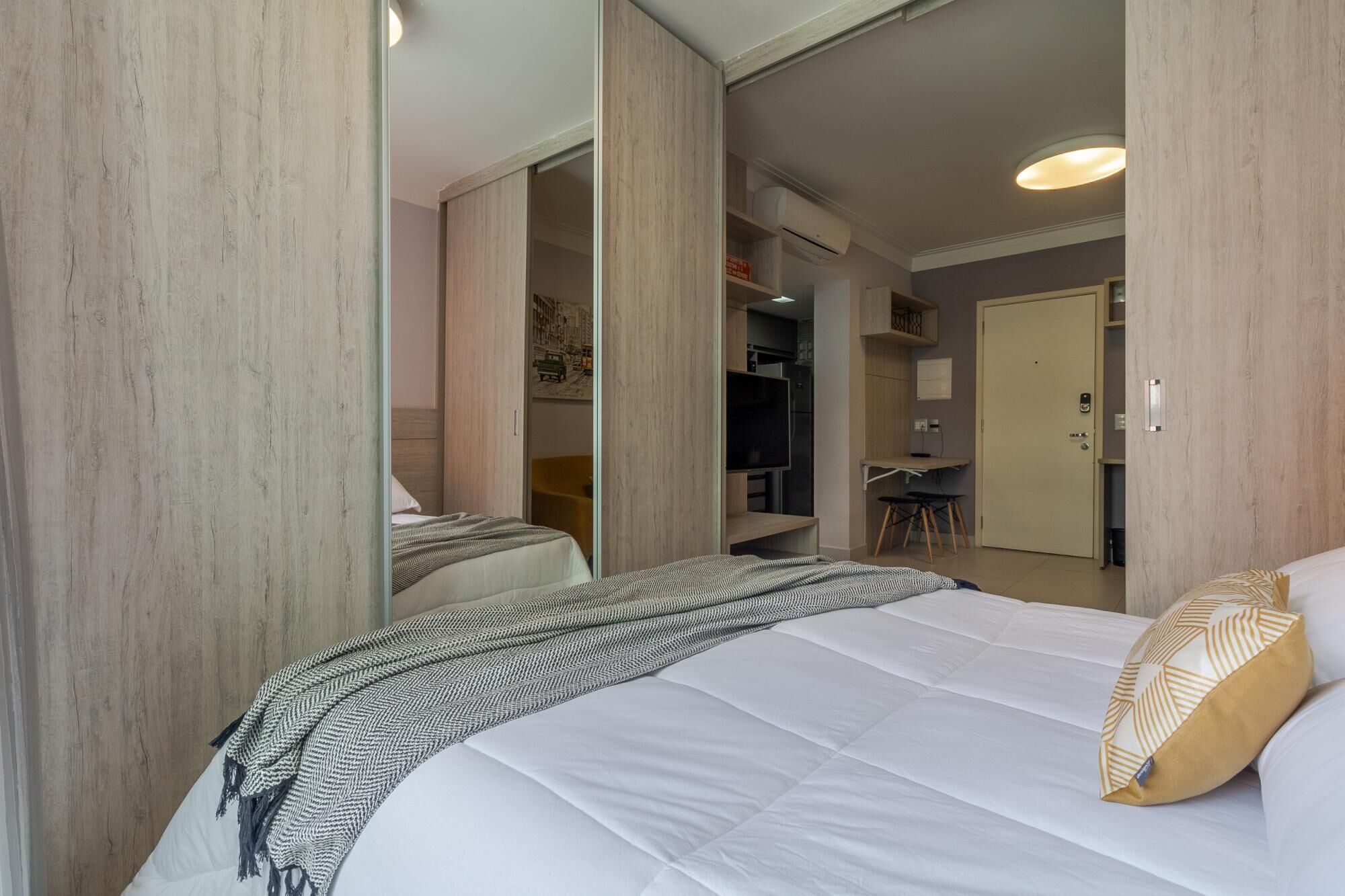 Um quarto com cama, guarda-roupa, escrivaninha e cozinha compacta.