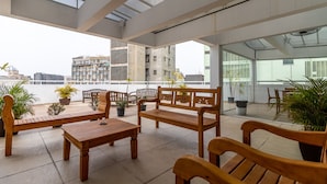 An outdoor seating area with wooden furniture and potted plants, overlooking a cityscape. - Av0703 Studio Avanhandava (São Paulo)