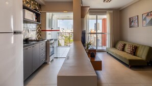 A modern kitchen with a refrigerator, stove, and cabinets, a balcony with a view of the city, and a living area with a sofa and a TV. - Ycp2101 in S o Paulo (São Paulo)