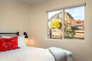 Ein Schlafzimmer mit einem Bett, einem Fenster mit Blick auf eine gebirgige Landschaft und einem roten Kopfkissen.