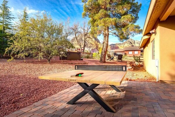 An outdoor patio area with a wooden table and benches, surrounded by trees and a brick pathway.