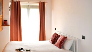 A bedroom with a wooden ceiling, a white bed, two red pillows, a small pink stool, and a patterned rug. - Our Happy Place Detached vacation home with garden (Mandello del Lario)