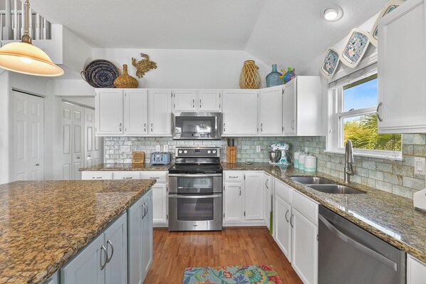 A modern kitchen with white cabinets, granite countertops, stainless steel appliances, and decorative items on the walls. - Relax, Play, Fish, Crab - Birds, Beach and incredible Sunsets - Sleeps 10 to 11 (Galveston)