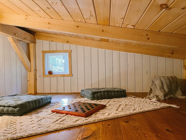 Een kamer met houten paneelwanden, een raam met uitzicht op bomen, een houten vloer en een schaakbord met ruitjes.