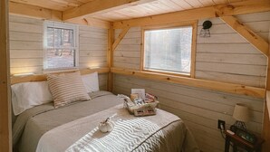 A cozy wooden cabin bedroom with a bed, a small bedside table, and a window with blinds. - COZY PSU Rustic Tiny Home and Fishing Retreat (Petersburg)