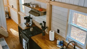 A kitchen with wooden cabinets, a stove, a sink, and a window. - COZY PSU Rustic Tiny Home and Fishing Retreat (Petersburg)