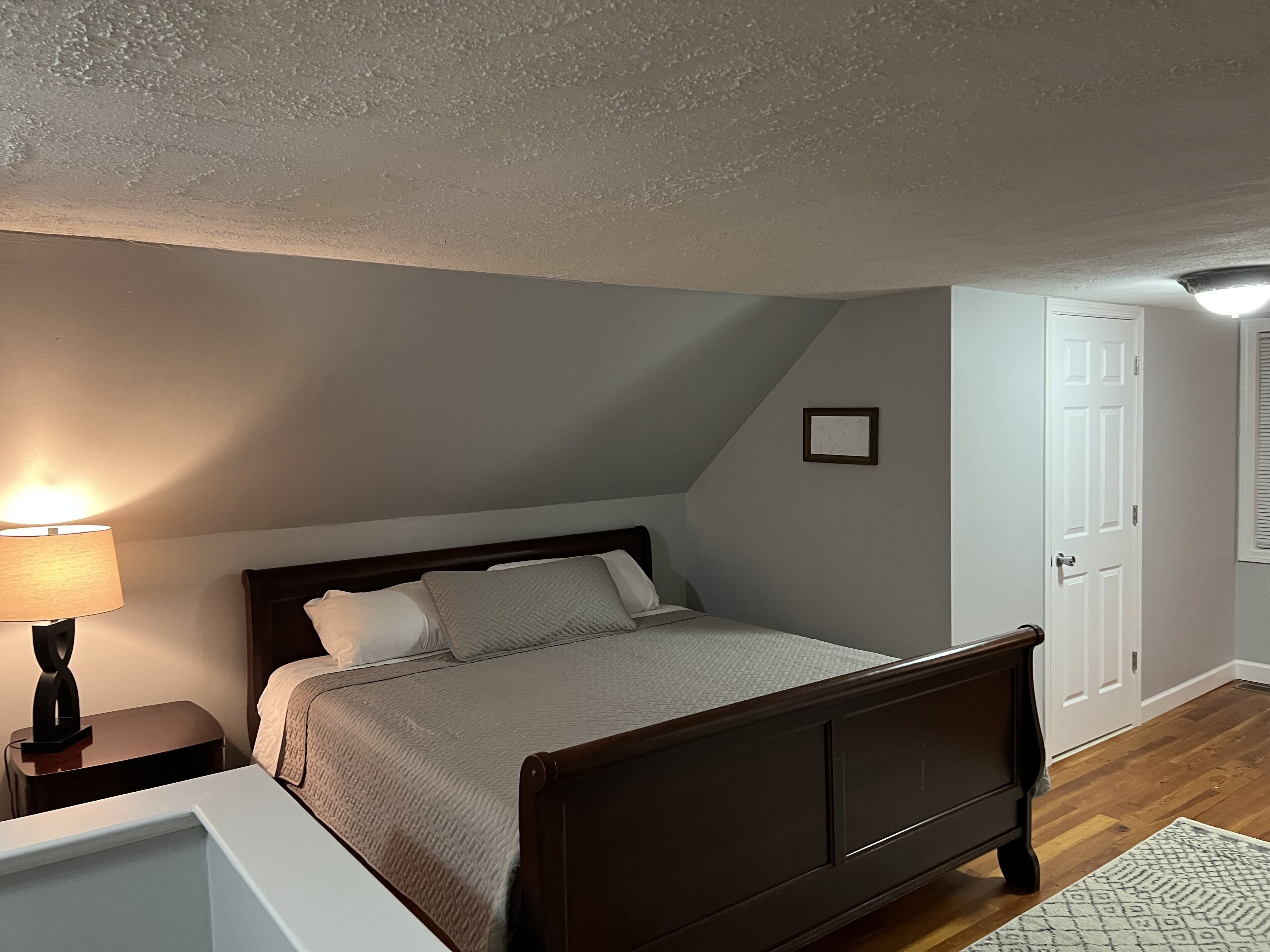A bedroom with a bed, bedside table, lamp, and a door.