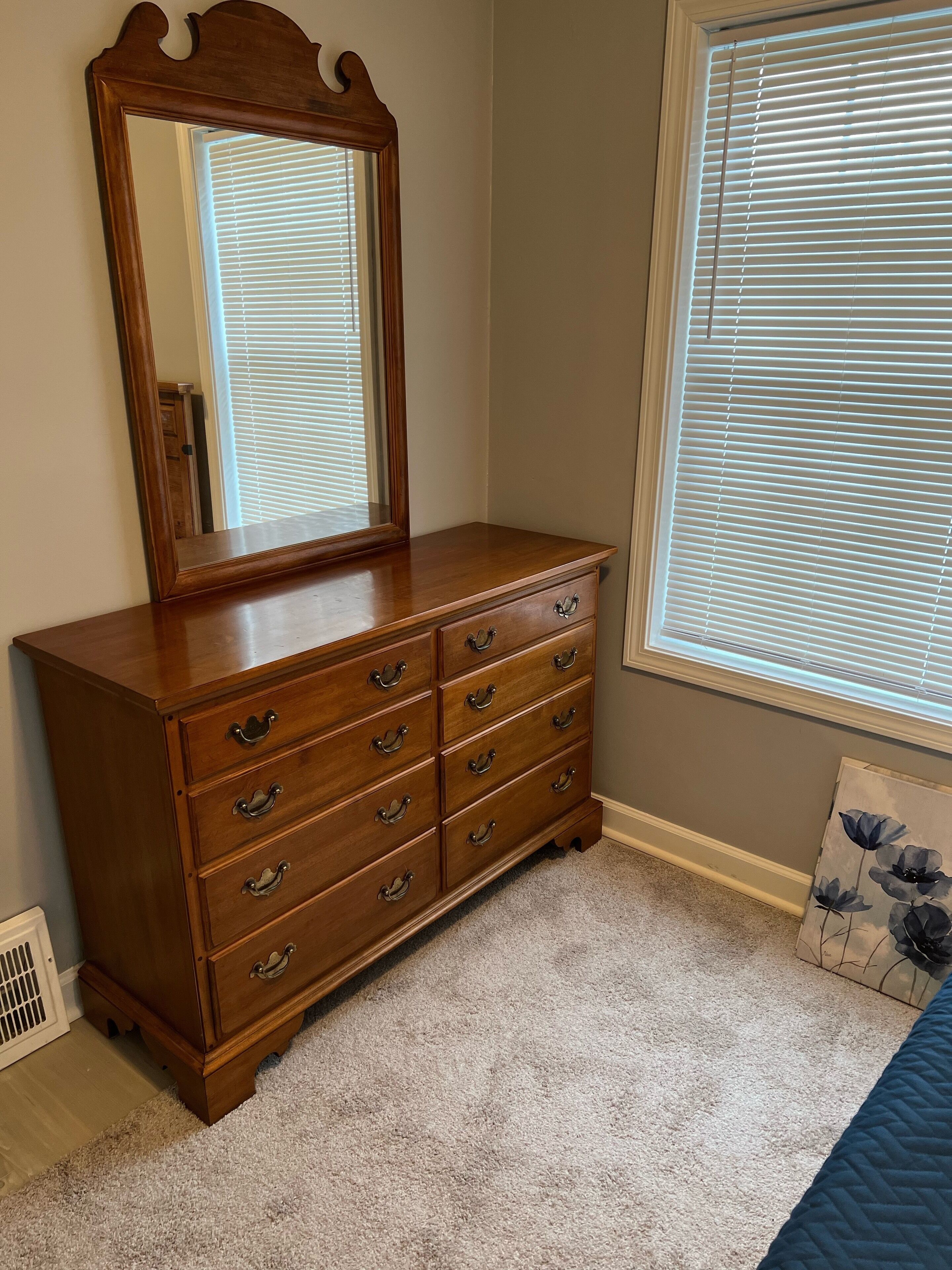 A wooden dresser with multiple drawers and a mirror, situated in a room with a window and a radiator.