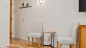 Een kamer met twee gestoffeerde fauteuils, een klein rond tafeltje en een wandplank met een decoratief metalen object.
