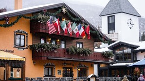 Ein Gebäude mit einem Balkon, der mit Flaggen geschmückt ist, einem Glockenturm und einem Schild mit der Aufschrift 'Hotel Gasthof'.