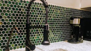 Een keuken met een spoelbak, een koffiezetapparaat en een achterwand van groene glazen tegels.