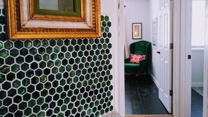 Een gang met een groene stoel, een inlijsting spiegel en een deur die naar een andere kamer leidt.
