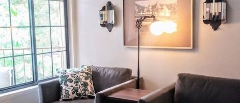 Ein modernes Wohnzimmer mit zwei Ledersofas, einem Couchtisch mit einem gewebten Korb, einem gerahmten Bild an der Wand und zwei Wandleuchten.