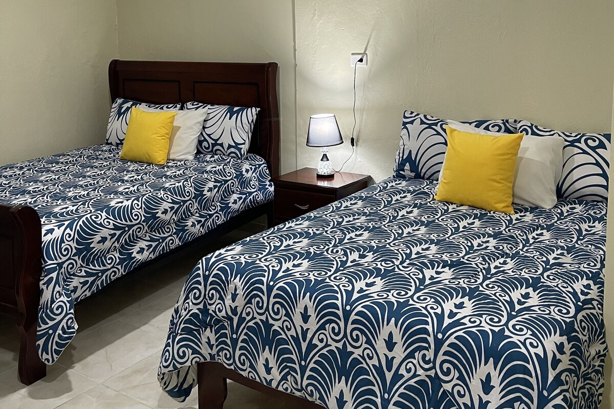 Two single beds with matching headboards and footboards, a bedside table with a lamp, and a wall-mounted light fixture.