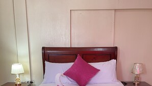 A neatly made bed with a pink pillow, a white towel with a flower, and a wooden headboard. - VBermor Hotel (Santo Domingo)