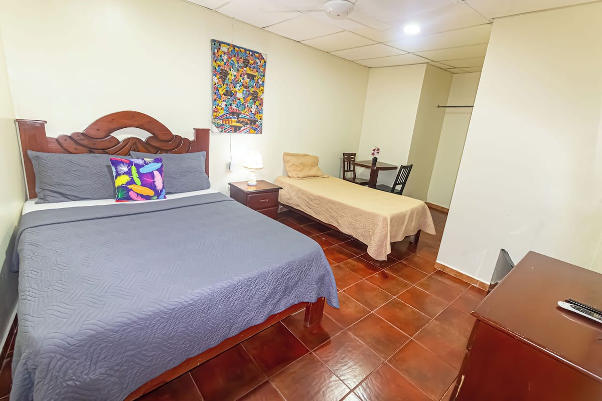 A hotel room with a large bed, a smaller bed, a desk, and a chair.