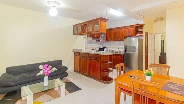 A modern kitchen with wooden cabinets, a dining table, and a black sofa. - VBermor Hotel (Santo Domingo)