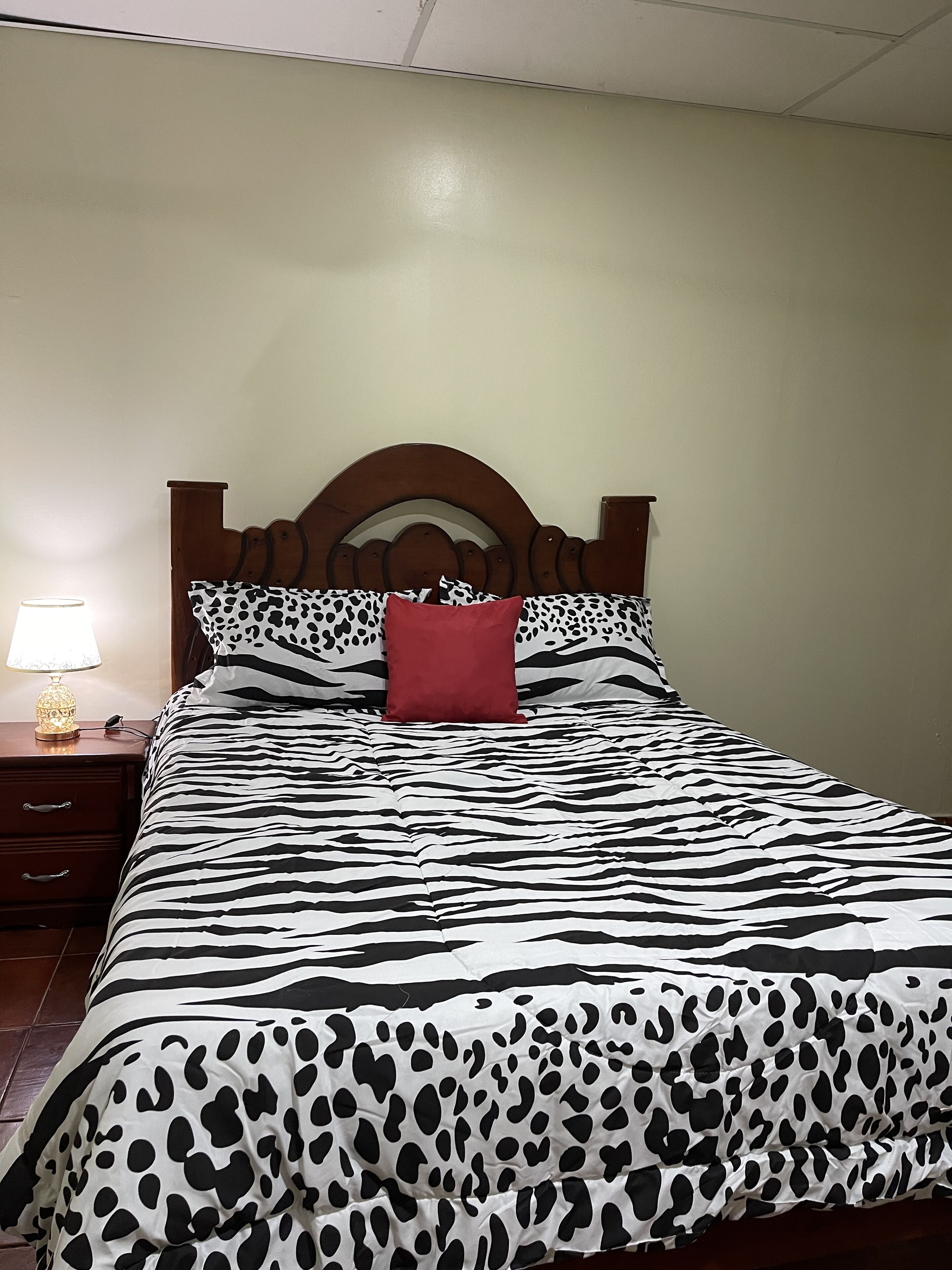 A bed with a zebra print bedspread, a wooden headboard, and a red pillow.