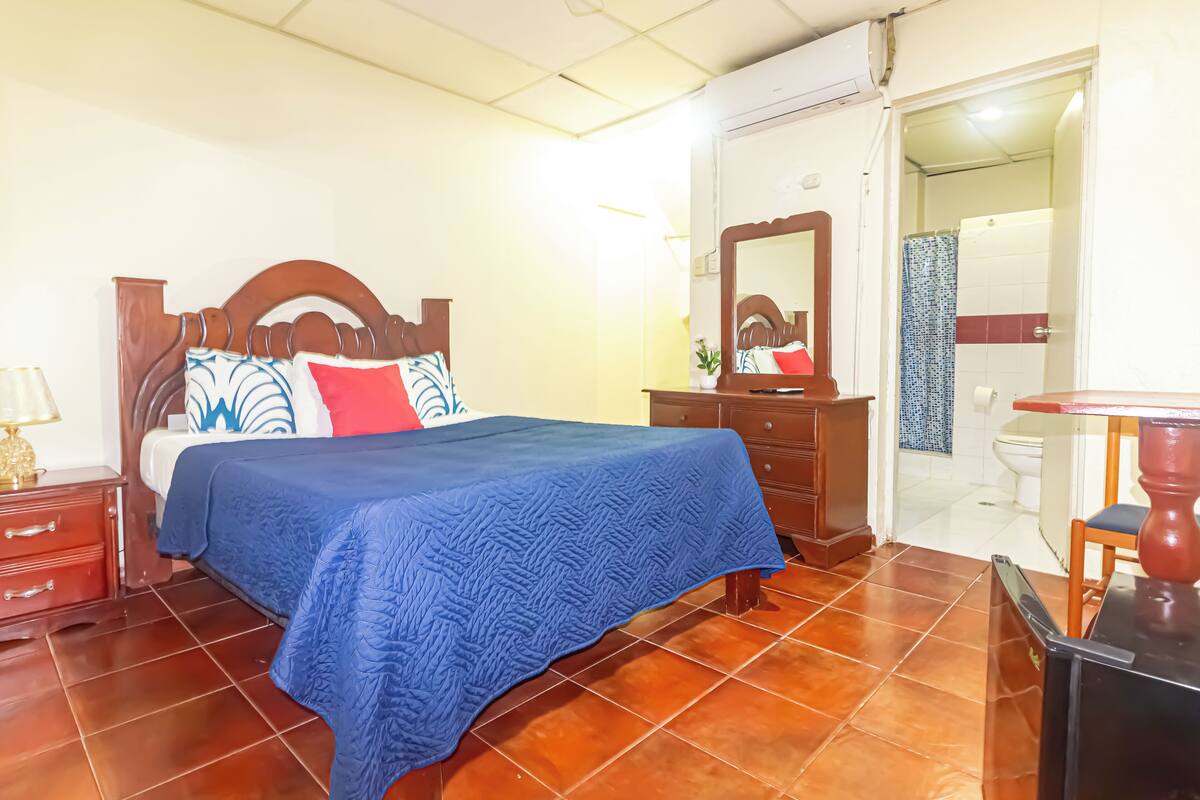 A bedroom with a wooden bed, a blue bedspread, a nightstand, a dresser, and a mirror.