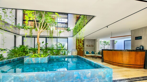 Un moderno vestíbulo de hotel con una piscina central, plantas de interior y un mostrador de recepción.