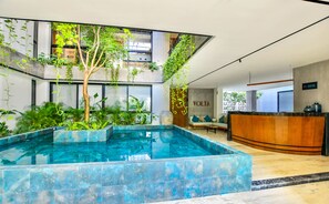 A modern hotel lobby with a central pool, indoor plants, and a reception desk. - Volta by Casago (Playa del Carmen)