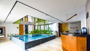 Un moderno vestíbulo de hotel con una recepción, una zona de piscina y plantas de interior.