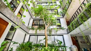 Un atrio moderno con un árbol central, rodeado de abundante vegetación y un techo alto con plantas colgantes.