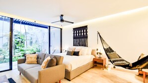 Un dormitorio moderno con cama, sofá, hamaca y un amplio ventanal con vistas a la vegetación.