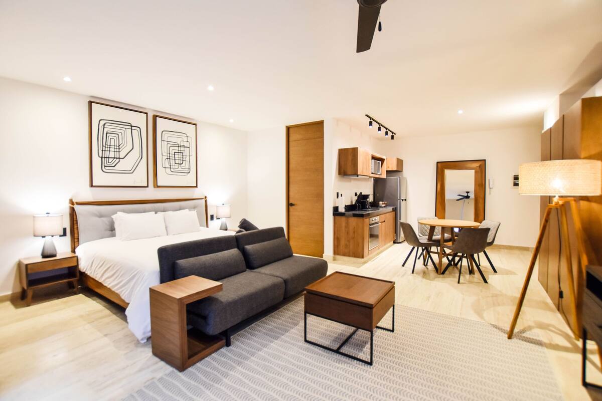 Habitació d'hotel moderna amb un llit, un sofà, una taula de cafè i una zona de menjador amb cadires i una taula.