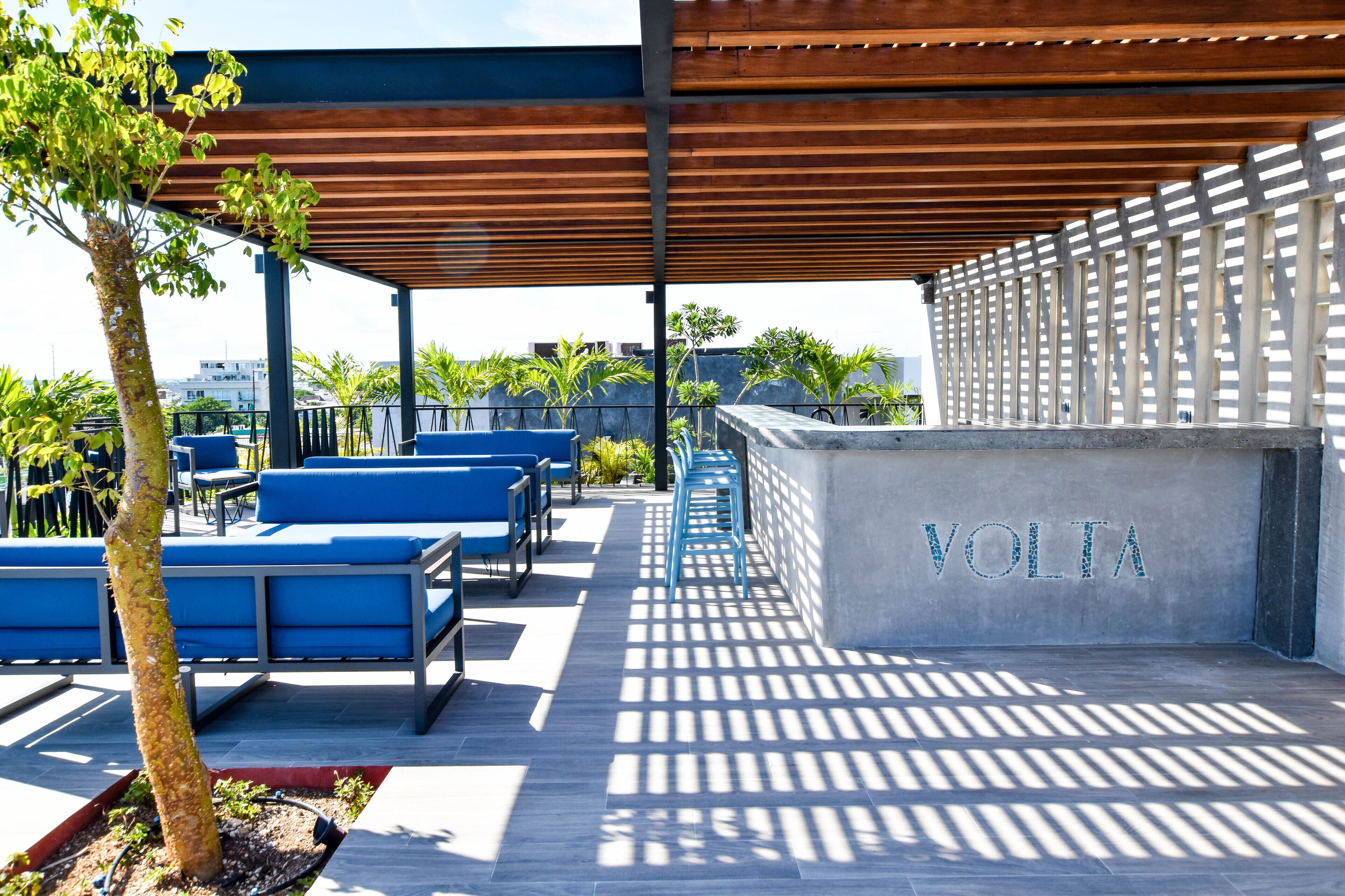 Un espace extérieur aménagé avec des chaises bleues et un mur en béton sur lequel est inscrit le mot « VOLTA ».