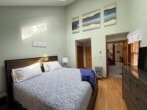 Une chambre à coucher avec un lit, des tables de chevet, une commode, un téléviseur et des œuvres d’art accrochées au mur.