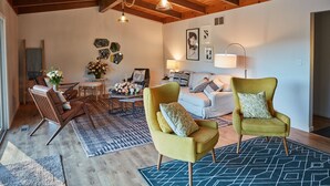Ein gemütliches Wohnzimmer mit Holzbalken, einer Couch, zwei Sesseln, einem Couchtisch und einem Teppich.