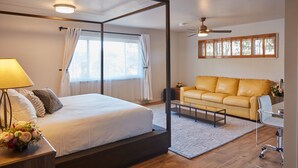 Ein modernes Schlafzimmer mit Himmelbett, einer Couch, Deckenventilator und großen Fenstern mit Vorhängen.