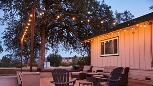Eine Terrasse im Freien mit Korbmöbeln, Lichterketten und einem großen Baum.