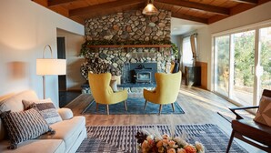 Ein gemütliches Wohnzimmer mit Kamin aus Stein, gelben Ohrensesseln und einer Couch.