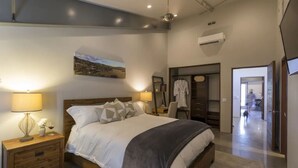 A modern bedroom with a large bed, bedside lamps, a nightstand, a wardrobe, and a mirror.