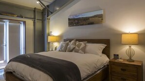A bedroom with a bed, bedside lamps, a nightstand, and a painting on the wall.