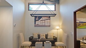 A modern living room with a dark sofa, two armchairs, a coffee table, and a painting above the sofa.