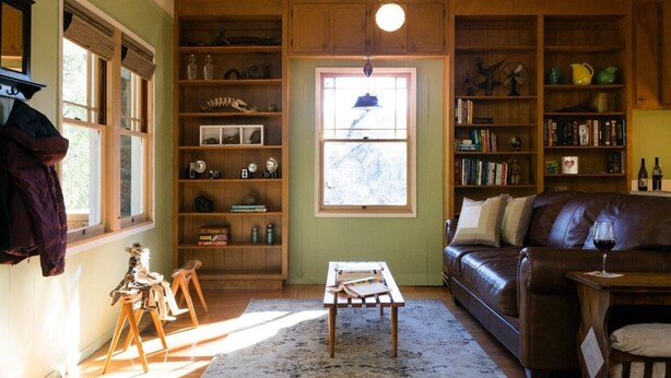 Een gezellige woonkamer met een leren bank, houten planken en een groot raam.