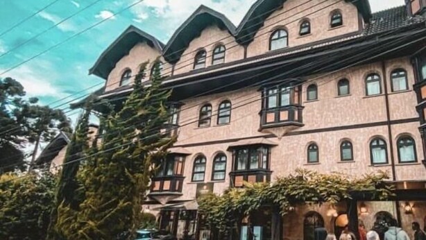 A multi-story building with a traditional architectural style, featuring a central entrance with a canopy and a log fence. - Campos Hotel do Sol (Campos do Jordão)