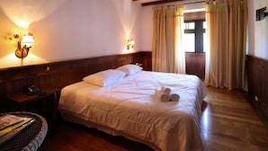 A hotel room with a large bed, wooden headboard, two wall-mounted lamps, and a window with curtains. - Campos Hotel do Sol (Campos do Jordão)